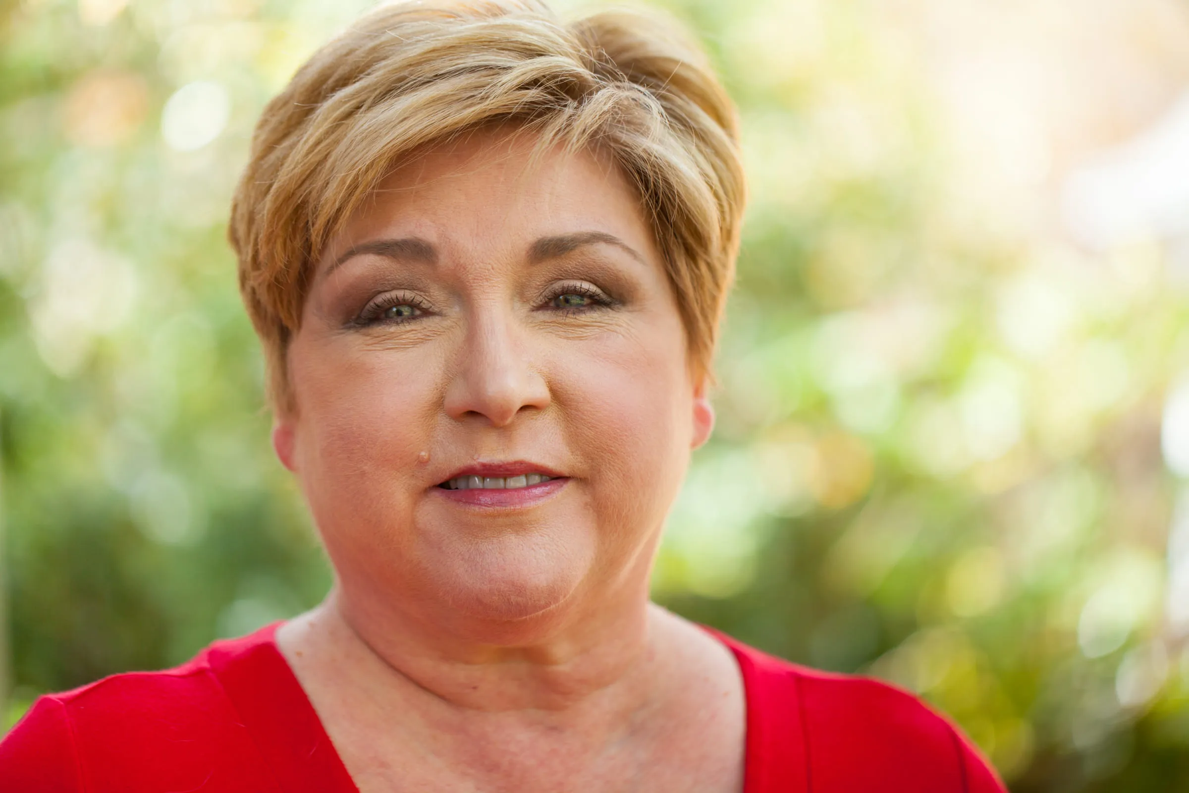 Portrait of Anita in a red top, smiling slightly, against a soft green garden background