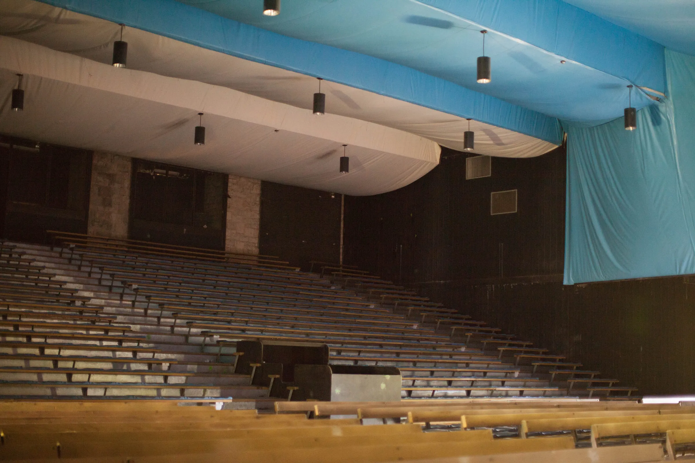 The inside of an abandoned theatre, rows of empty seats under a sagging blue tarpaulin ceiling
