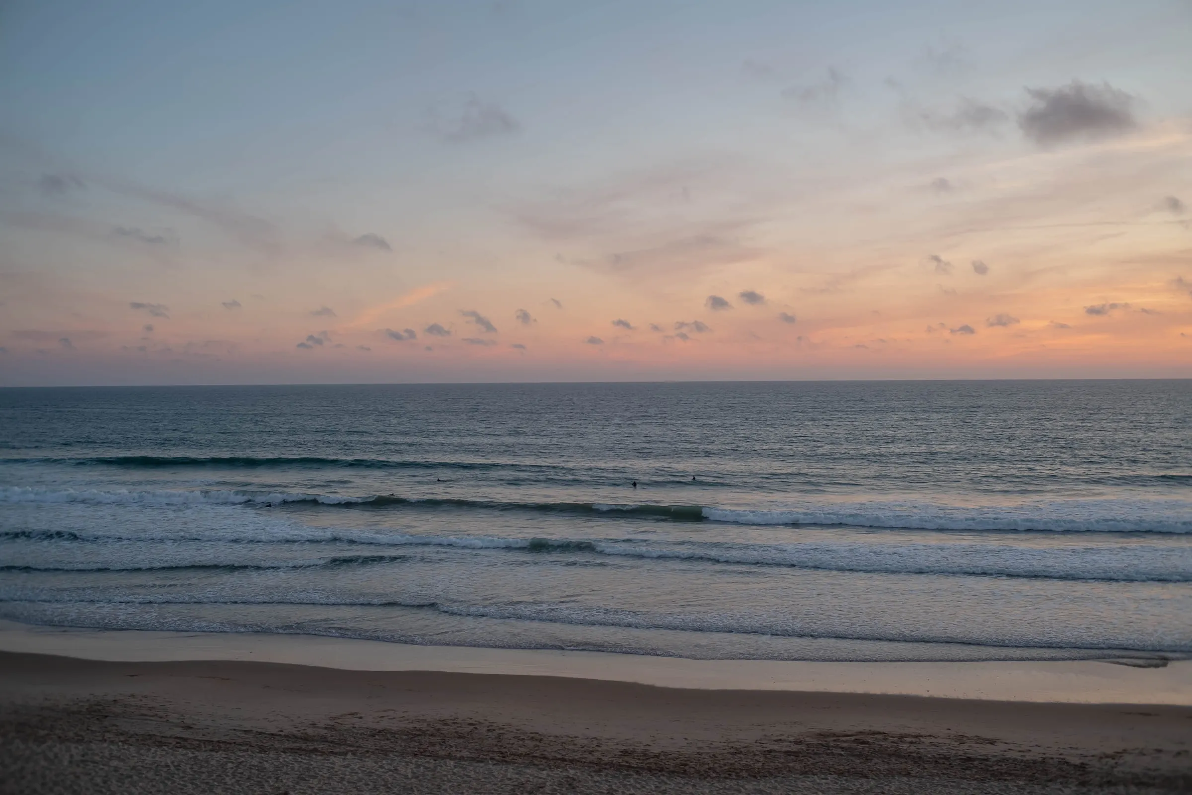 Empty beach and breaking surf under a pale pink and gold dawn sky