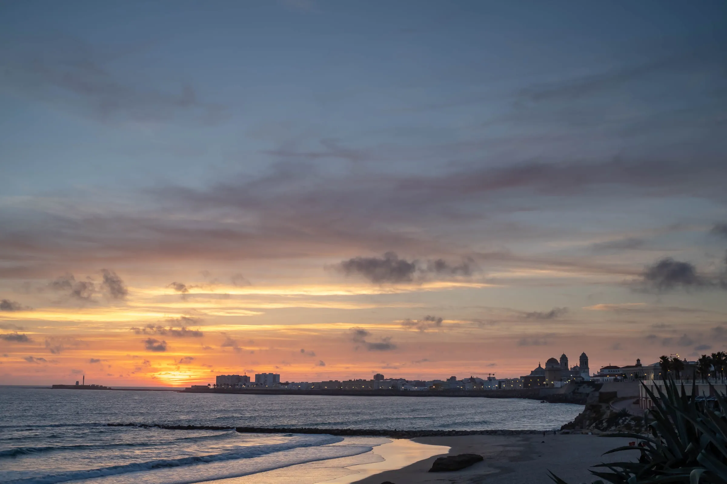 The sun setting behind the Cádiz peninsula, the city strung low along the horizon above the surf