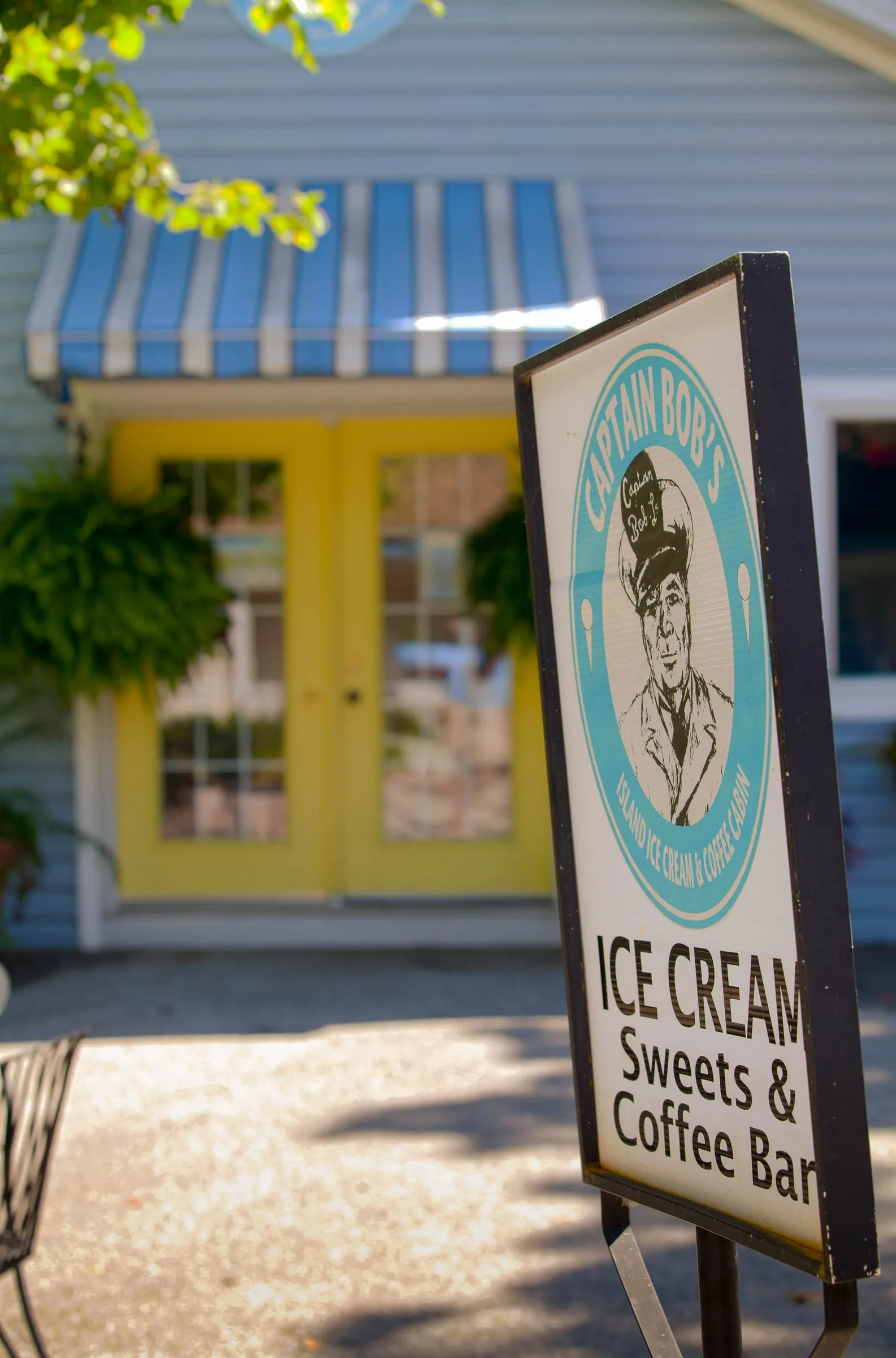 A sandwich board for Captain Bob's ice cream and coffee bar outside a yellow-doored shop