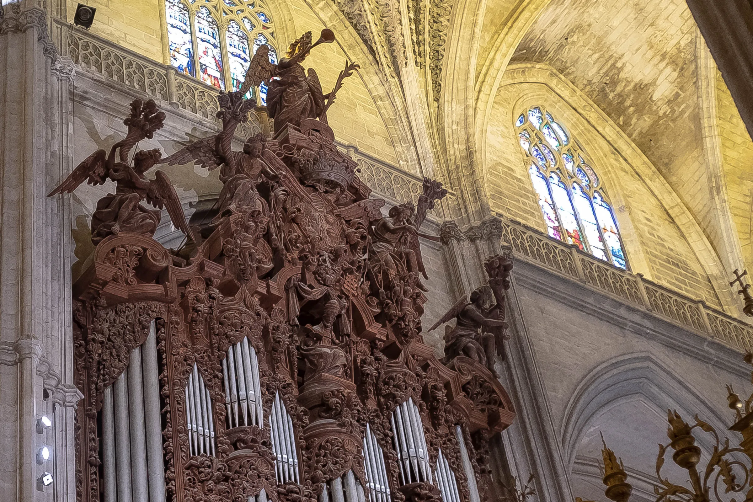 An elaborate carved wooden sculpture above the cathedral organ pipes, stained glass behind