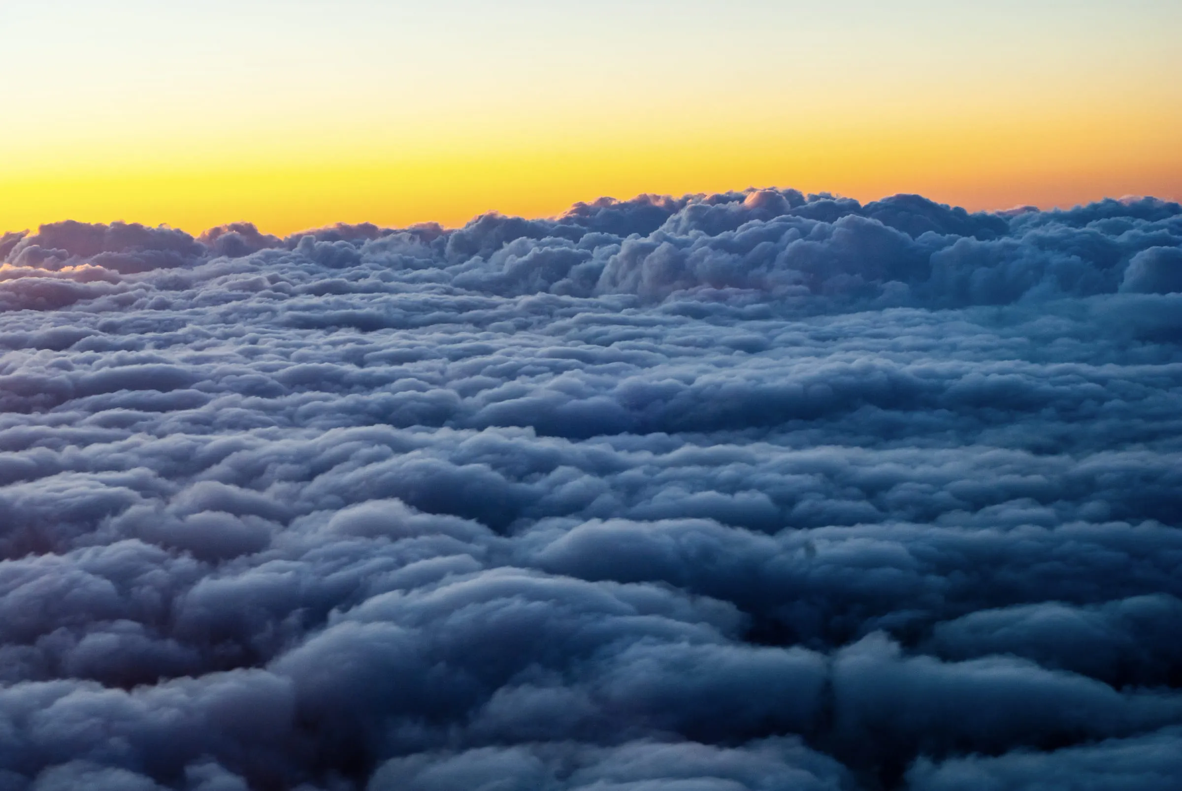 An unbroken deck of cloud seen from above at sunrise, gold light along the horizon