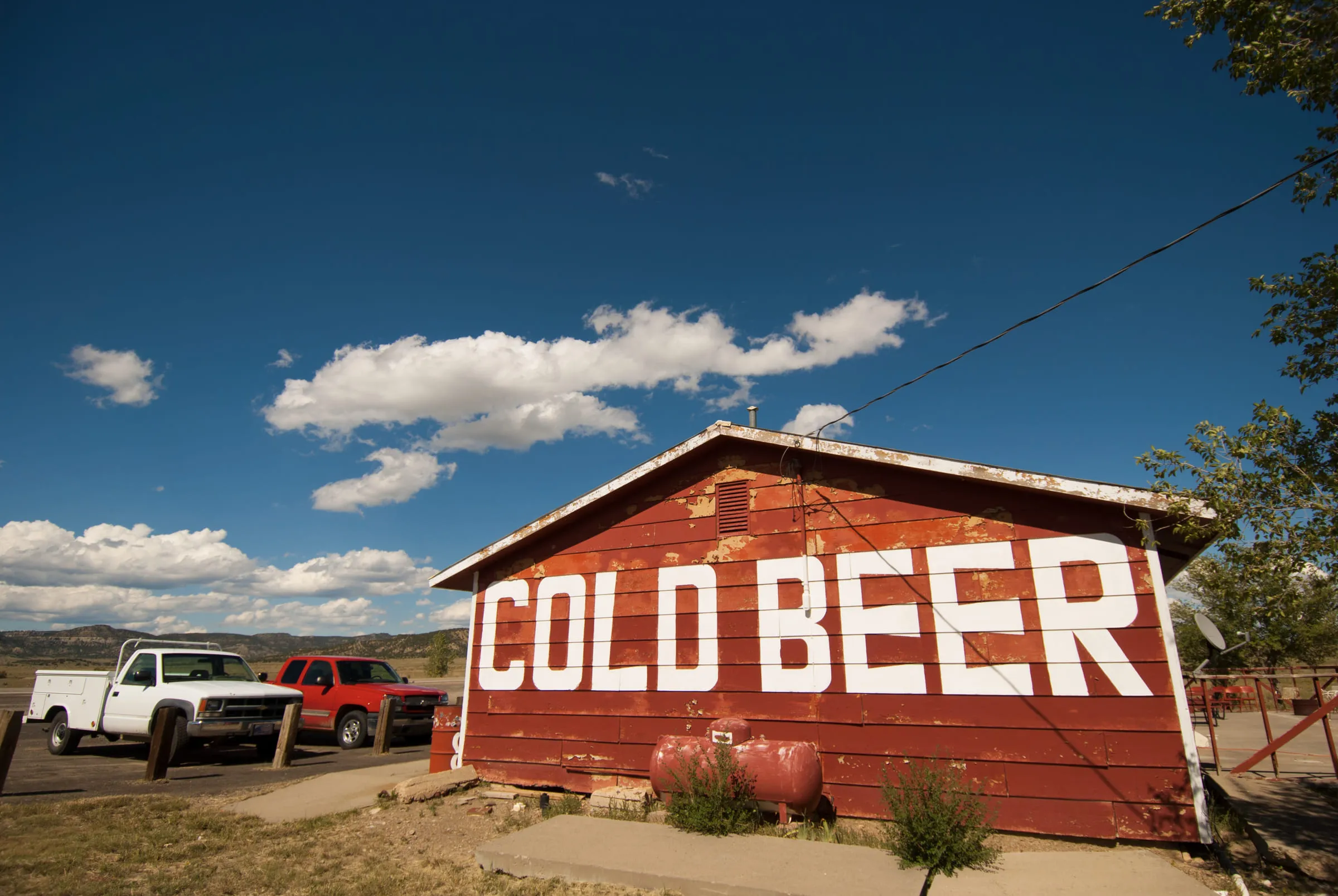 A long red barn with COLD BEER painted across it in tall white letters, pickup trucks parked at one end