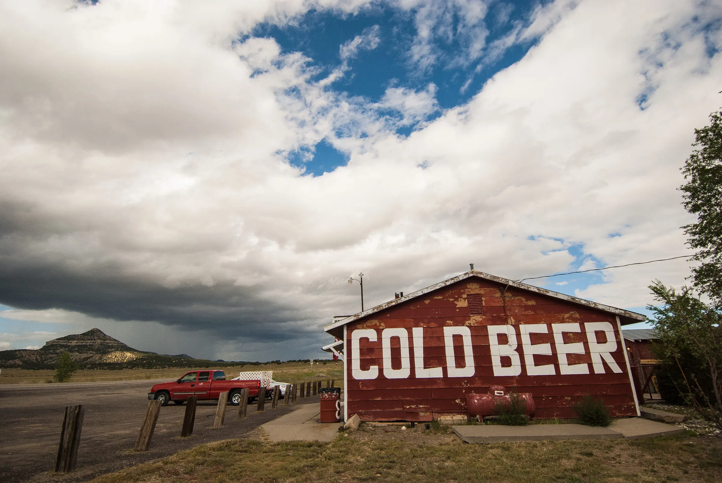 The COLD BEER barn seen from further back, a dark storm building over a flat-topped butte behind it