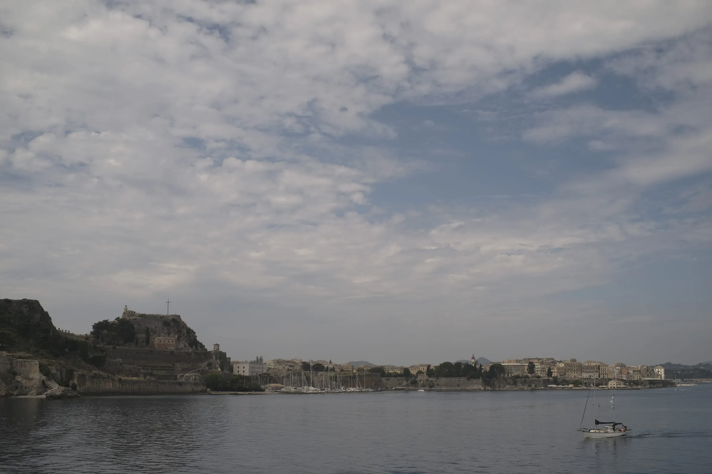 The Corfu waterfront in flat grey light, the fortress and old town low along the shoreline