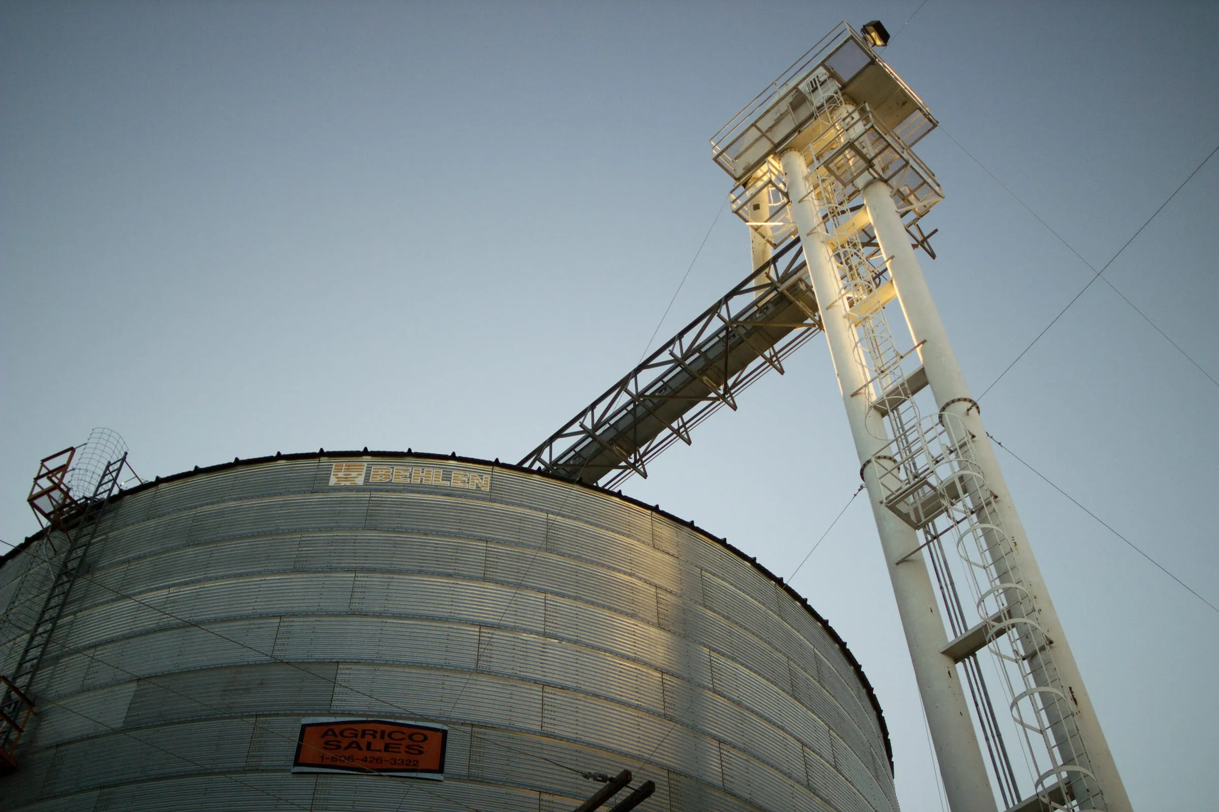 A corrugated steel grain bin and elevator leg shot steeply from below against a pale sky