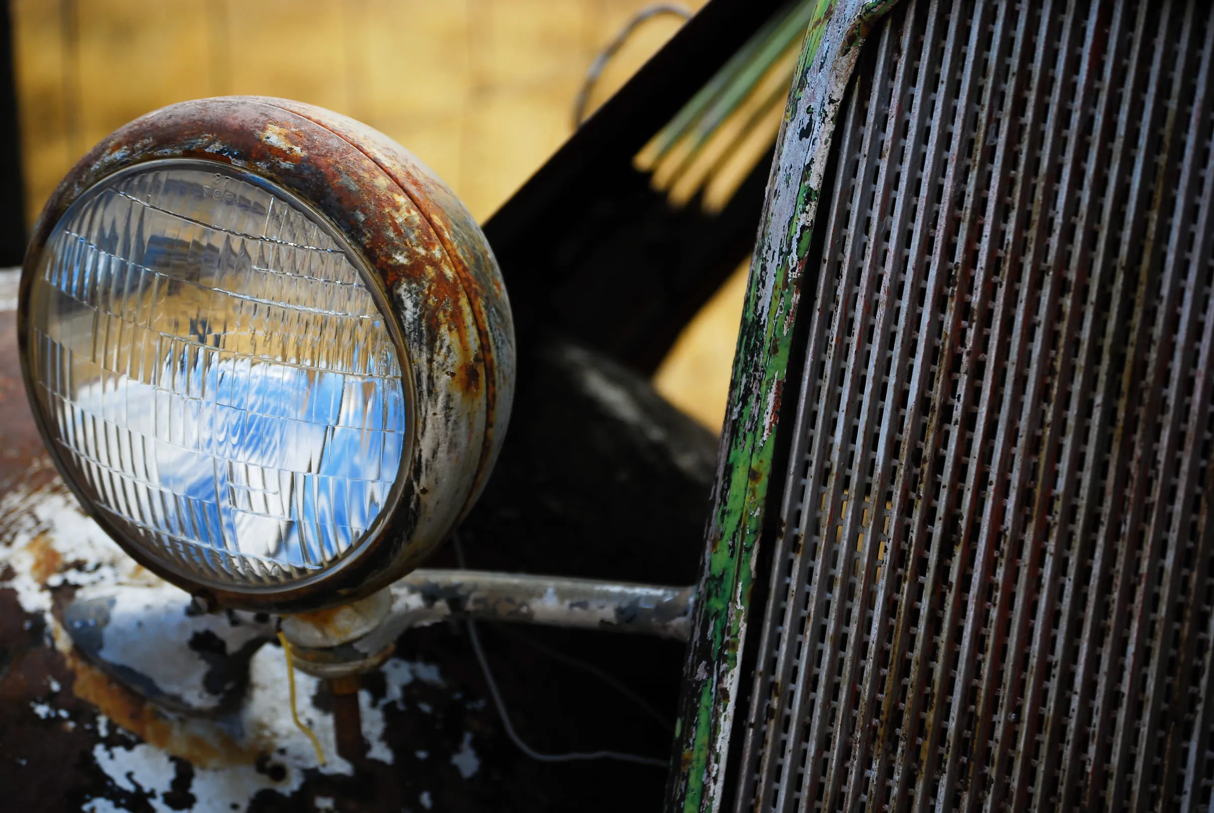 Close-up of a chrome headlamp on a rusting truck, its grille catching the light beside it