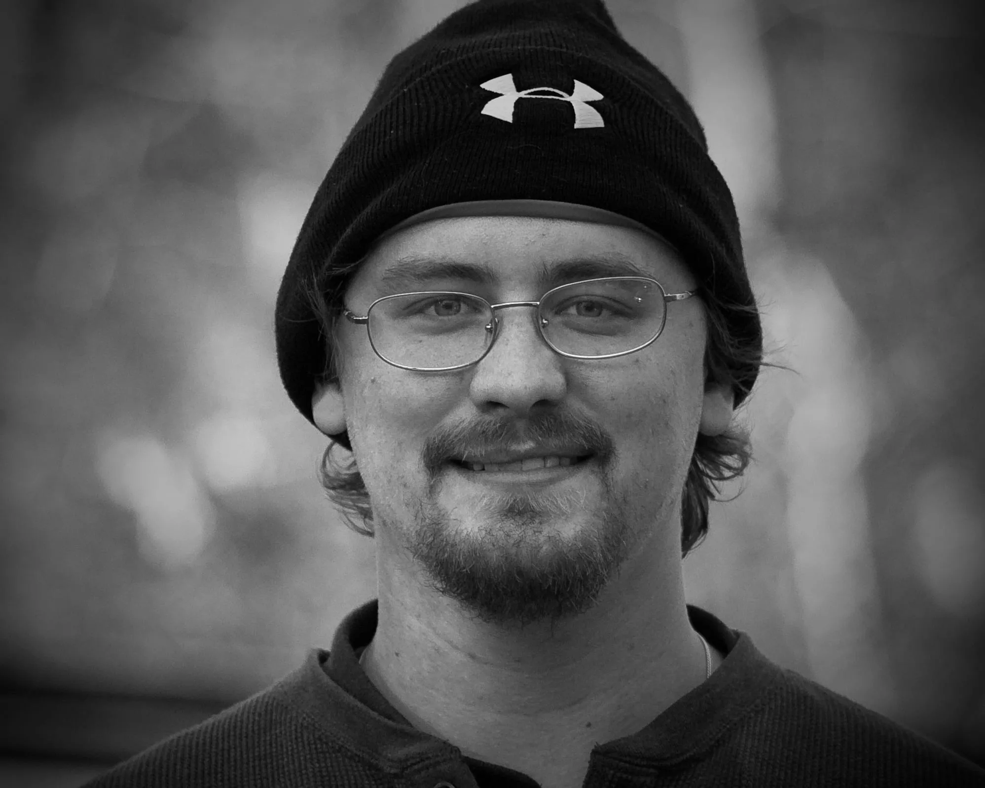 Black and white portrait of Justin in a knit beanie and glasses, smiling