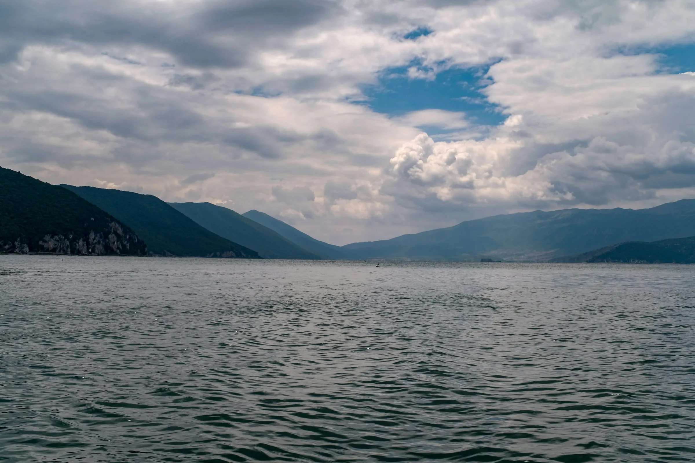 Lake Prespa under a tall build of cloud, steep green mountains falling to the water on both sides
