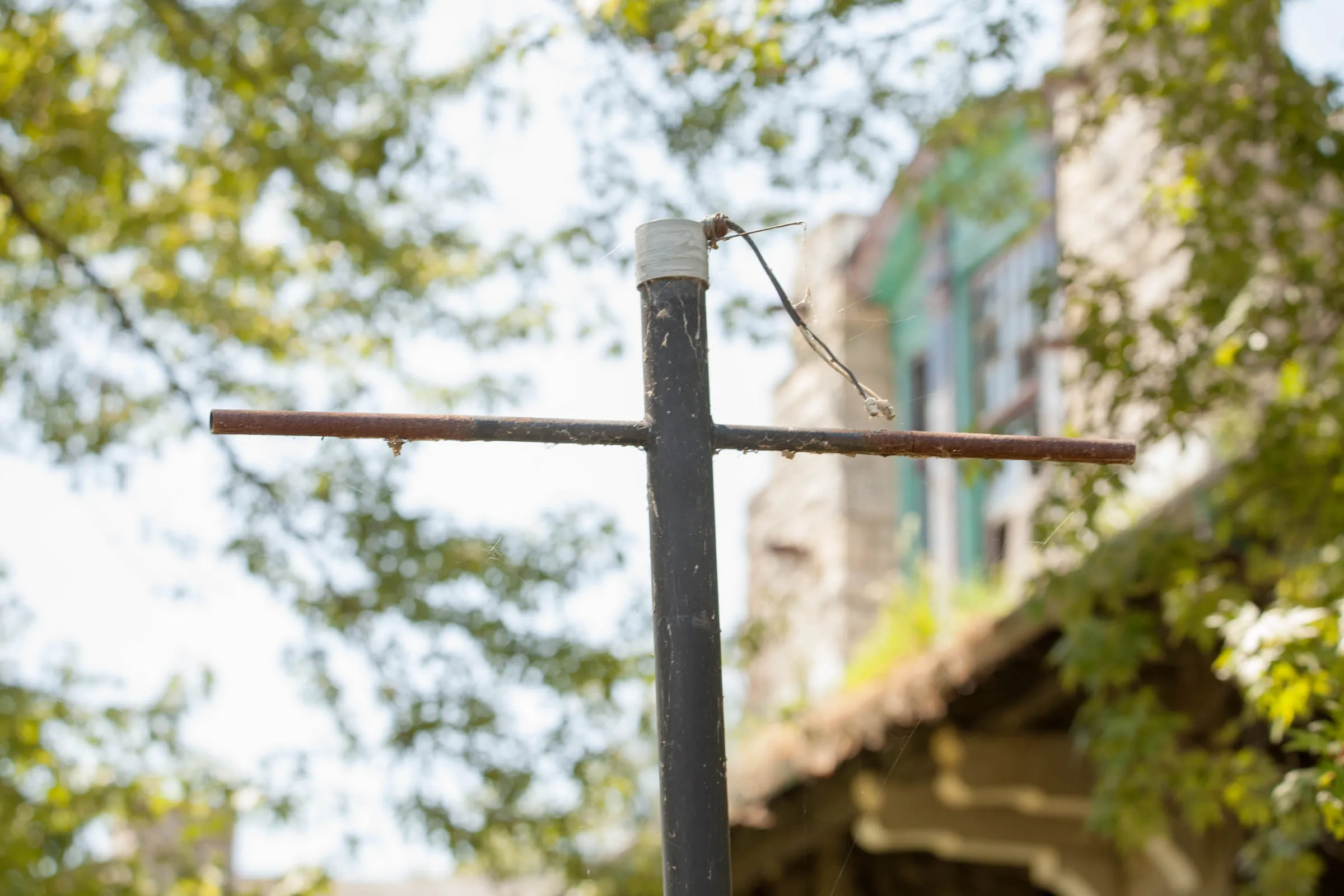 A bare metal lamp post crossbar with its fitting gone, seen from below against the tree canopy
