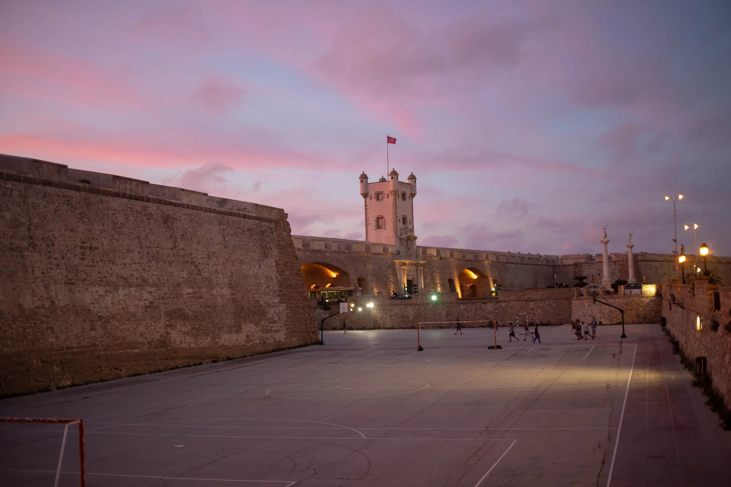 The Puertas de Tierra gate tower lit against a pink dusk sky, an empty plaza in front