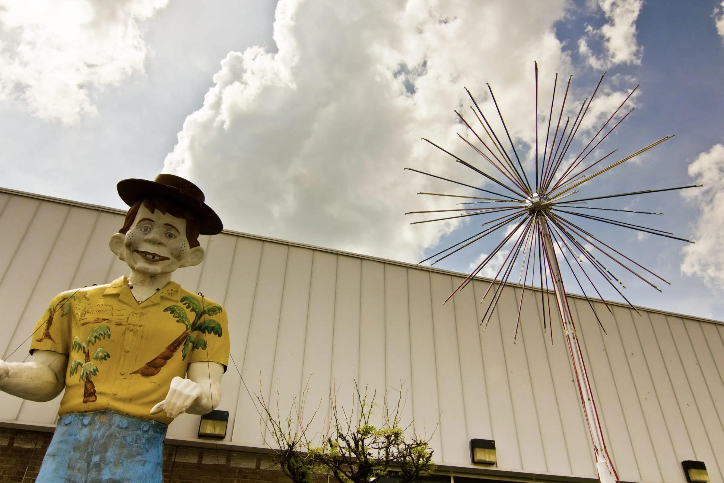 A fibreglass figure in a straw hat and Hawaiian shirt standing at the corner of a metal building