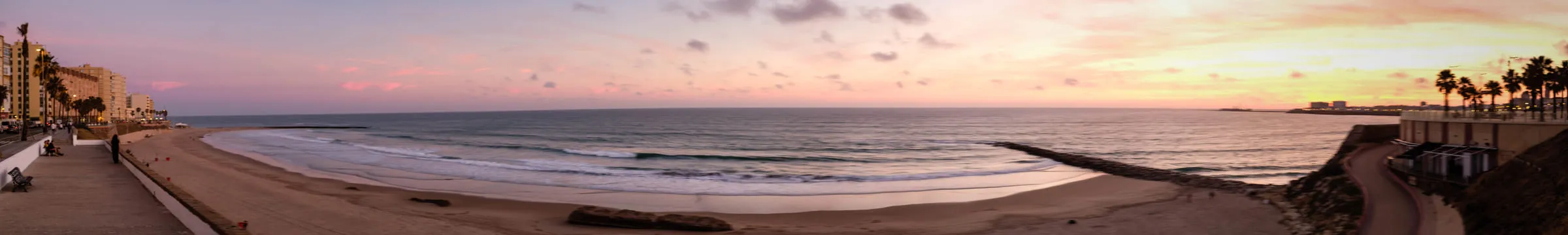 Wide panorama of the Cádiz beach curving away under a soft sunset