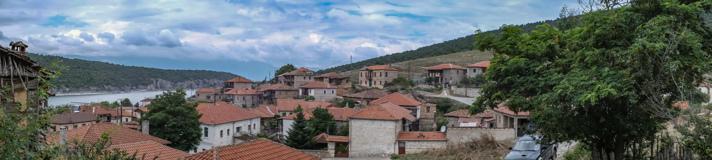 Red-tiled rooftops of Psarades stepping down toward the lake, a large tree to one side