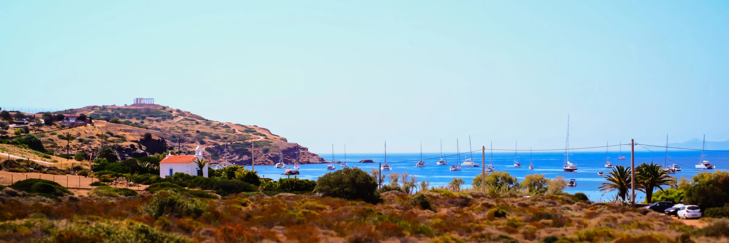A rocky headland town above a bay full of moored sailing boats, scrub in the foreground