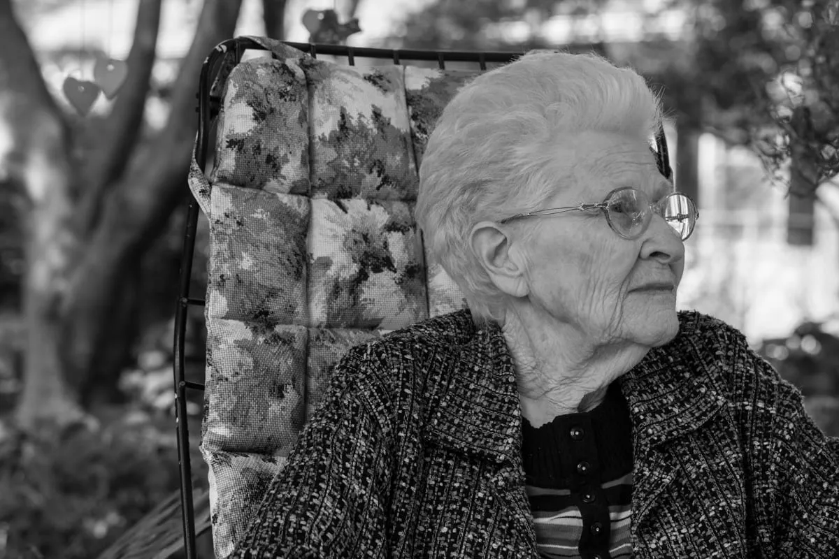 Black and white portrait of Ruth seated outdoors in a patterned coat beside a cushioned chair back
