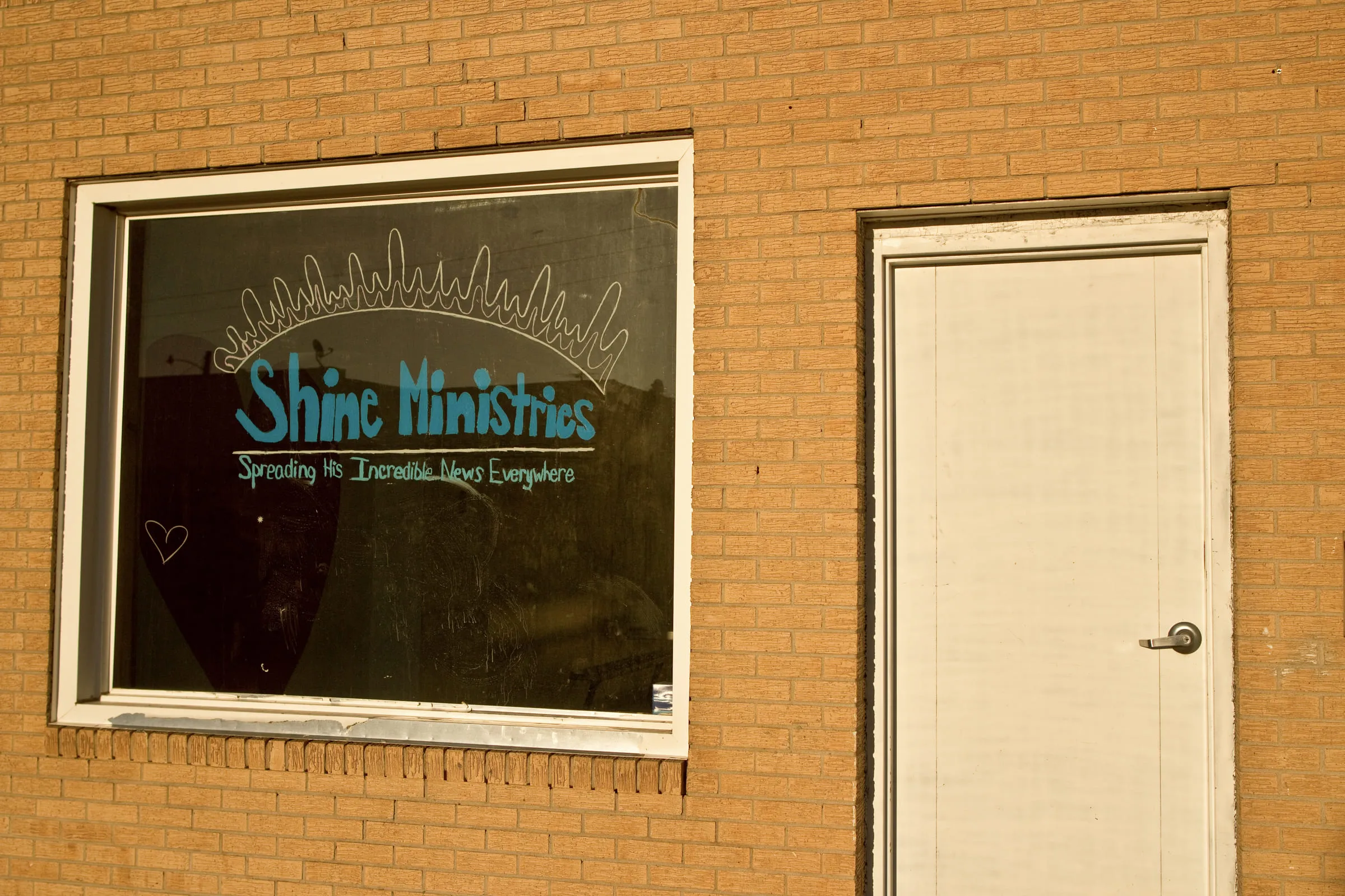 A brick storefront with "Shine Ministries" hand-painted on the window beside a plain white door