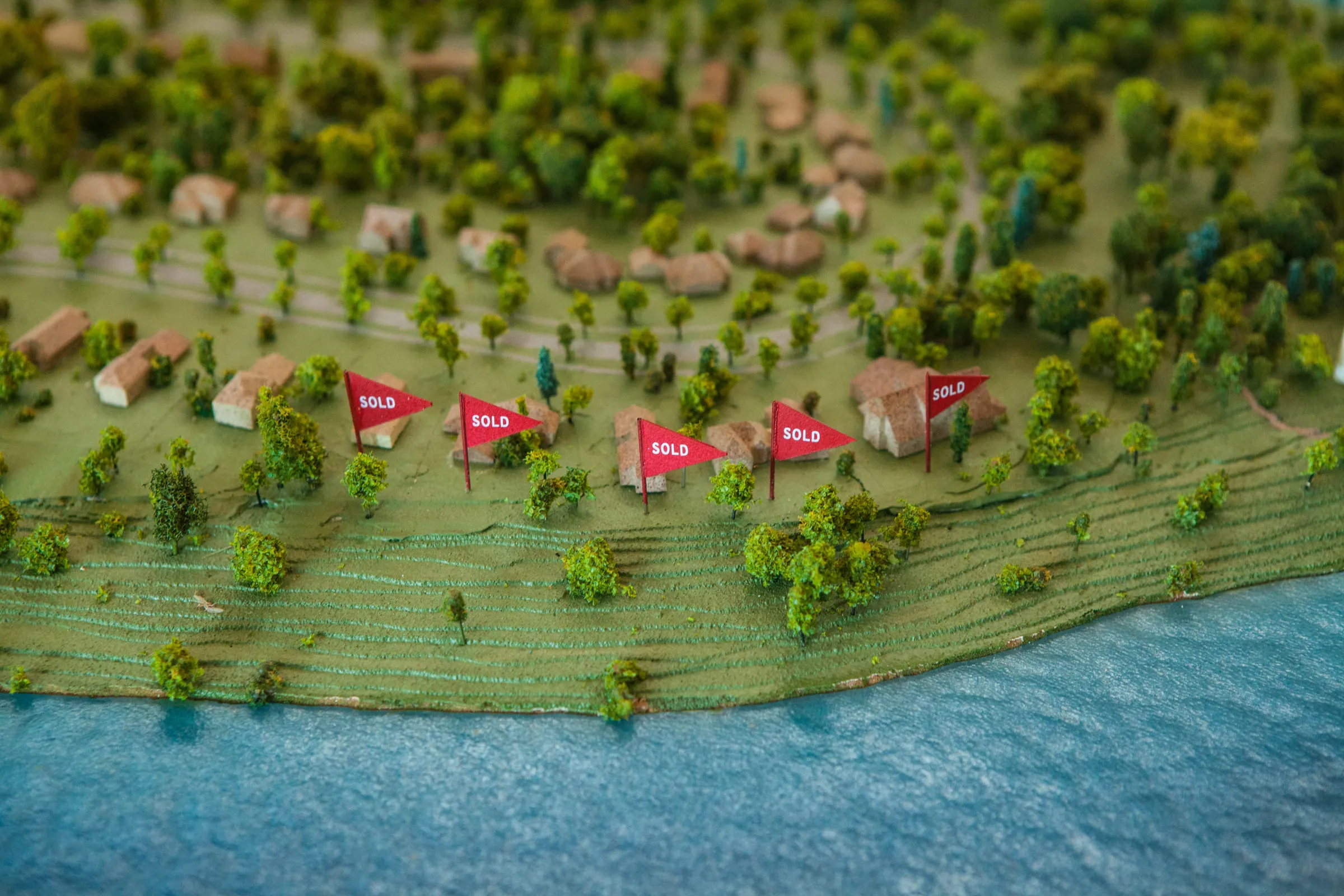 A closer view of red SOLD flags among the model's miniature houses and trees along the shore