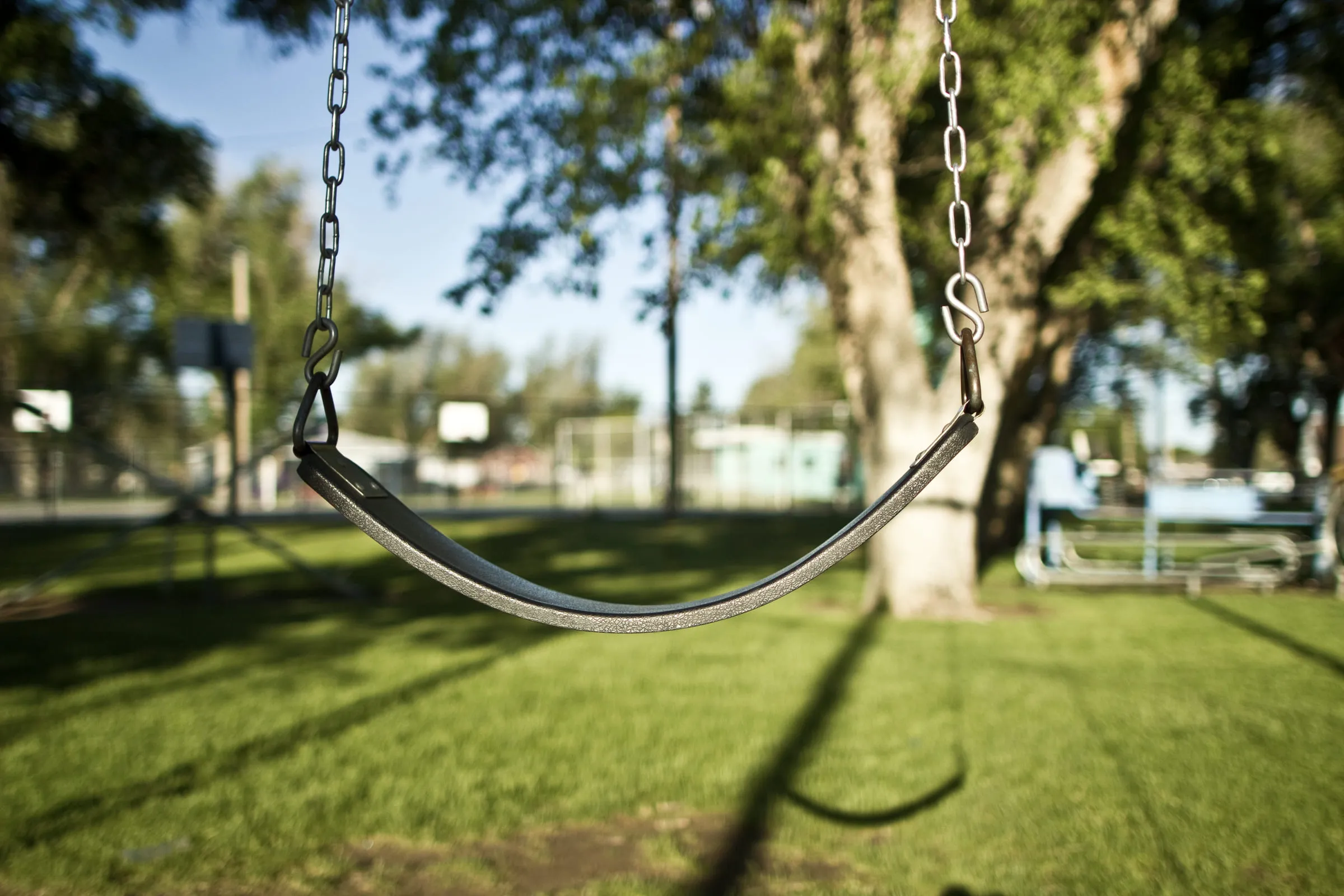 An empty playground swing hanging still in the shade of a tree
