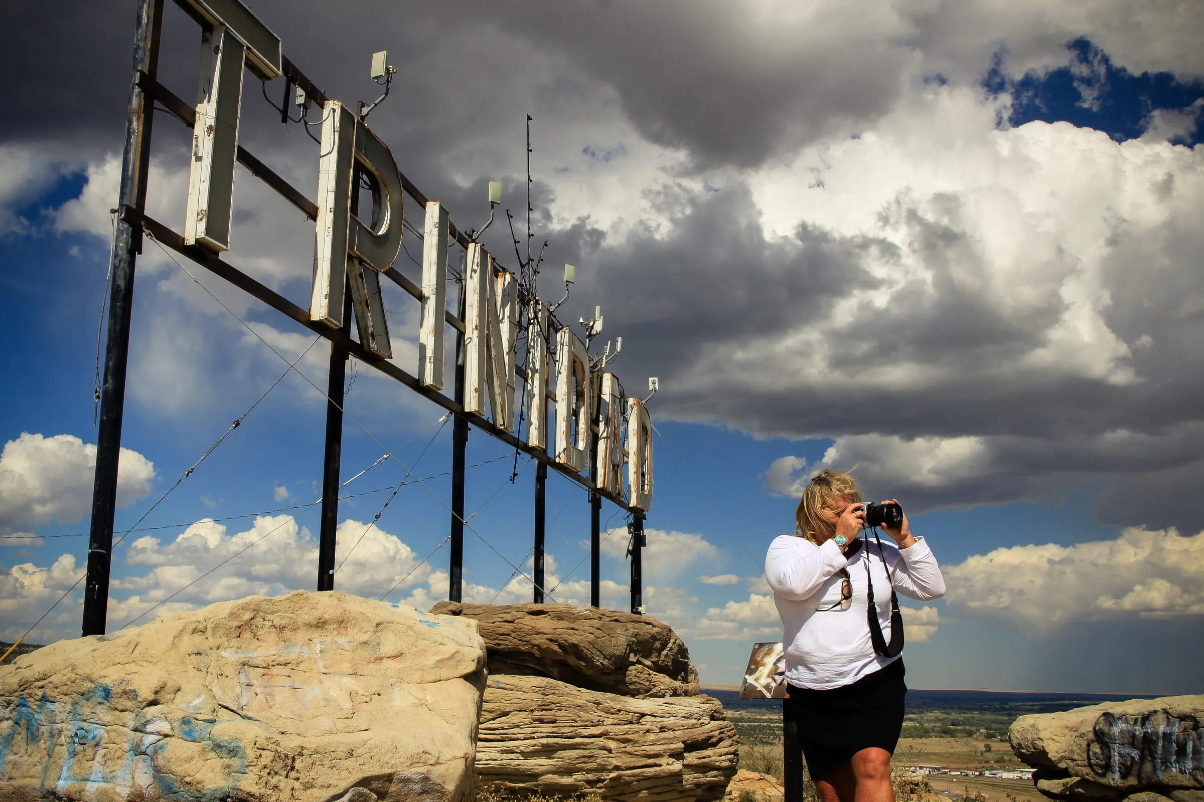 Teresa photographing from a rock outcrop beneath the large steel TRINIDAD hillside sign