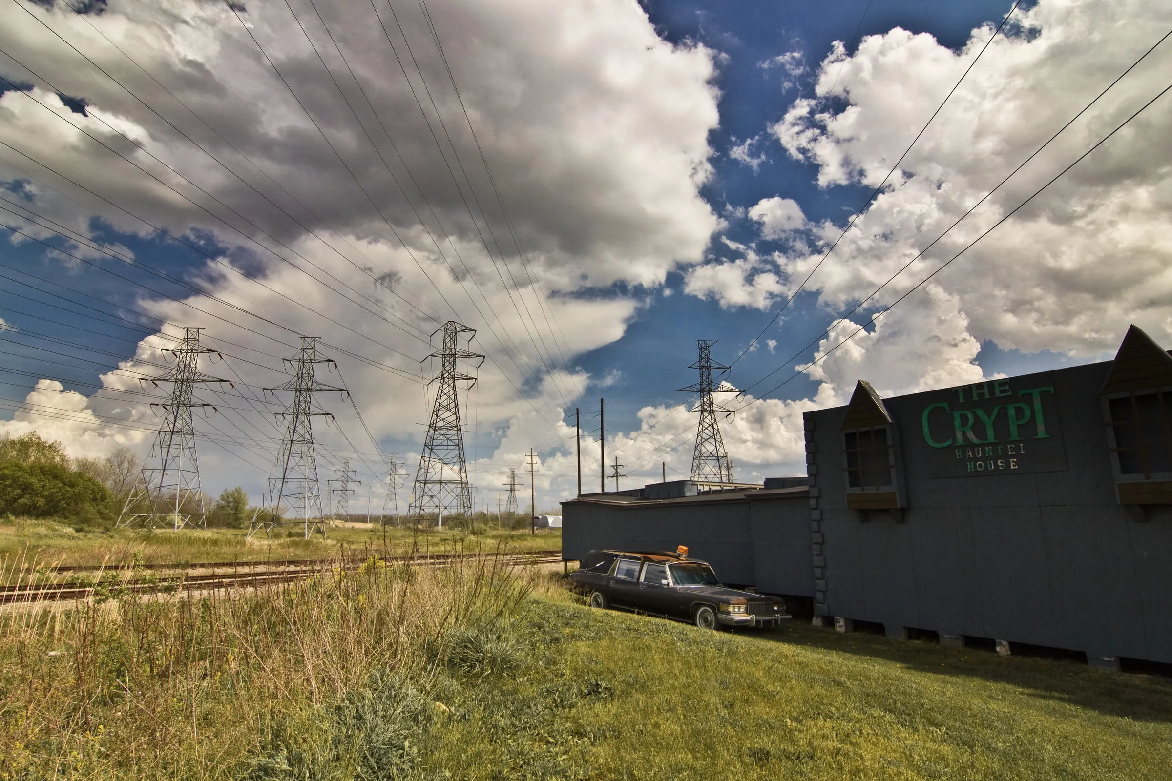 A dark building signed THE CRYPT beside a rail line, transmission towers marching away behind