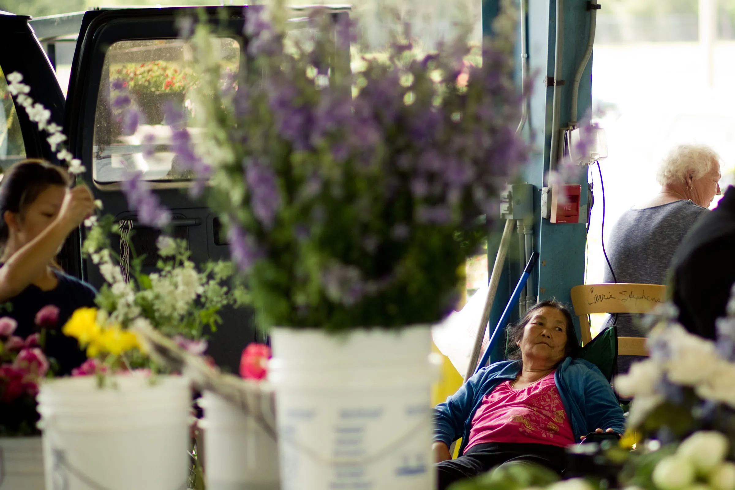 A market seller asleep in a chair behind buckets of flowers at the back of a van
