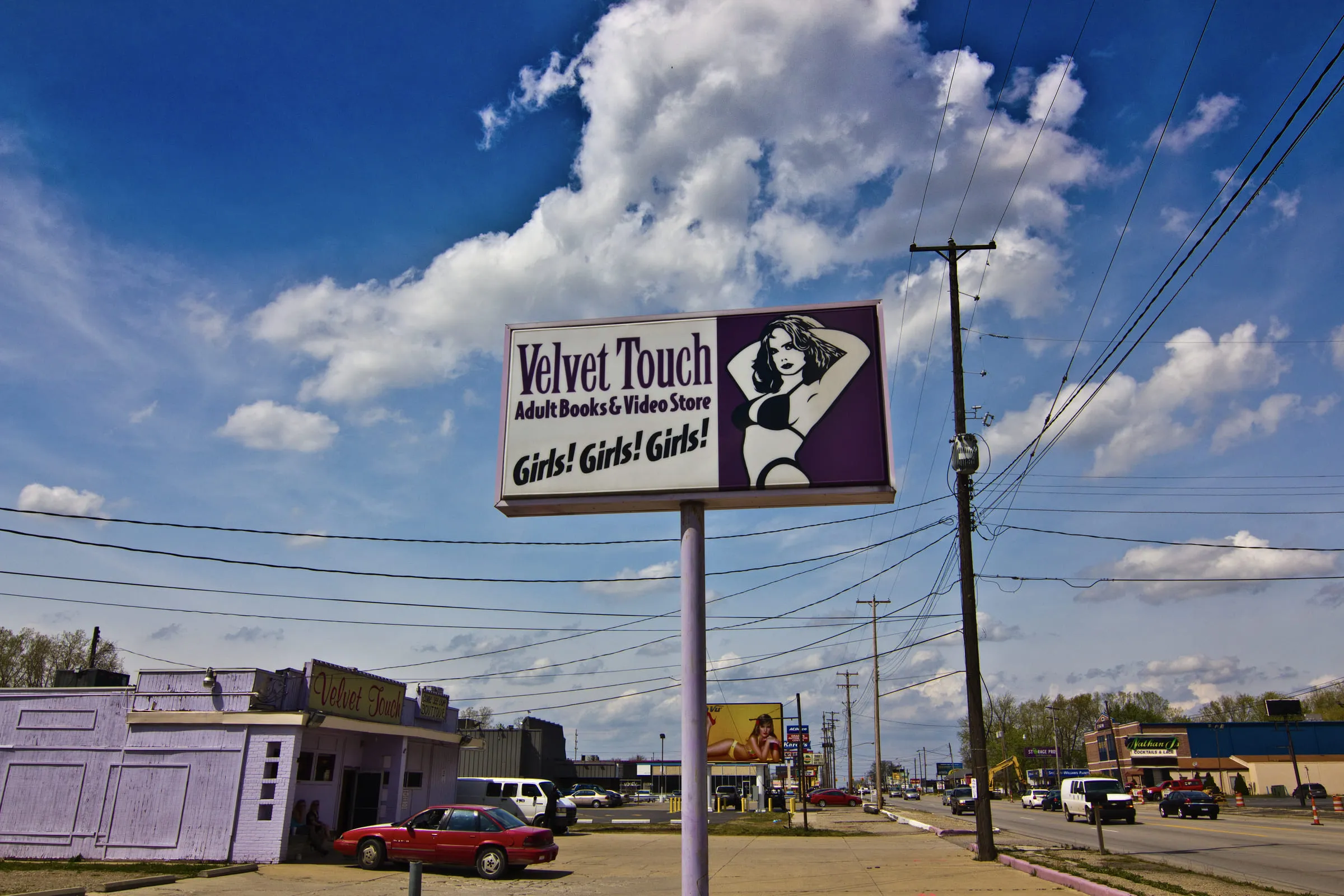 A roadside billboard for the Velvet Touch adult book and video store above a street of low buildings