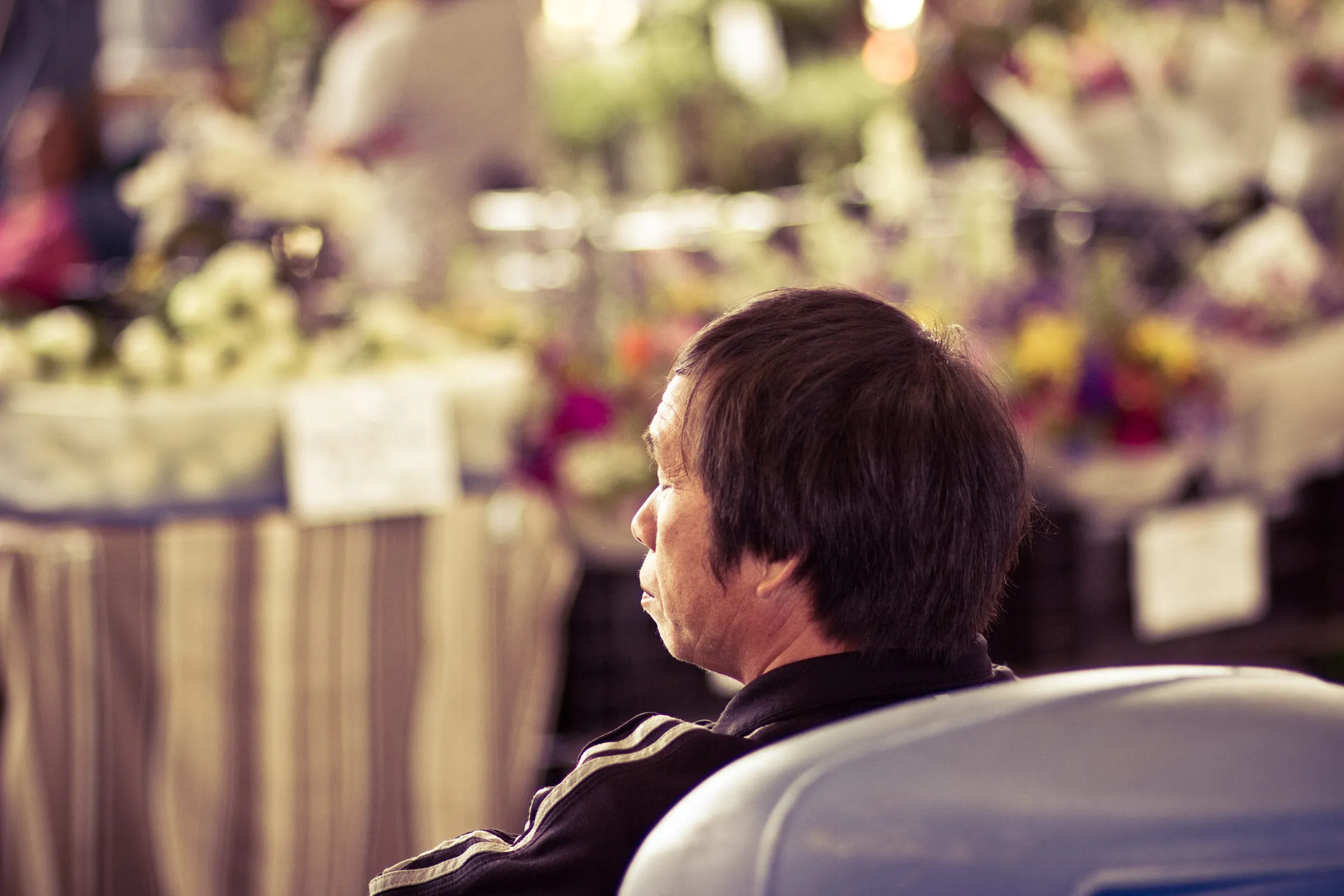 A vendor seated among buckets of cut flowers at a market, waiting for customers