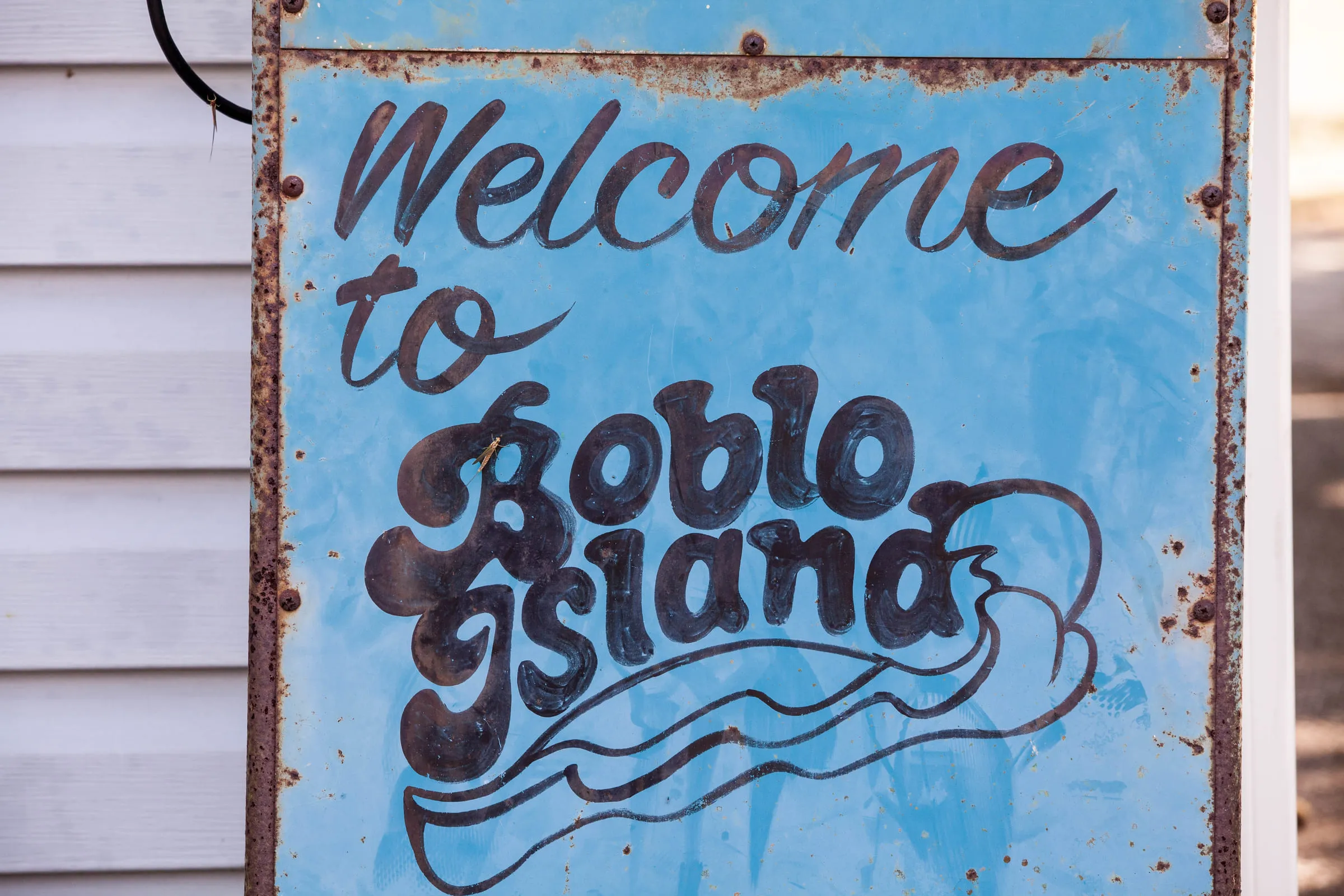 A rusted metal sign hand-lettered "Welcome to Boblo Island" in blue script