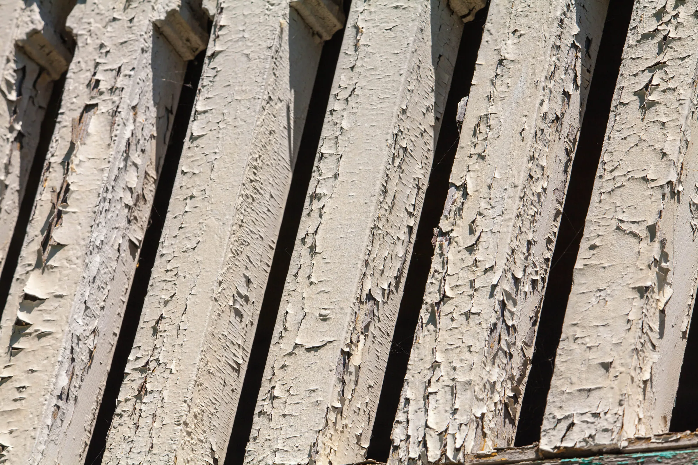 Close-up of thick white paint curling off a row of angled wooden boards