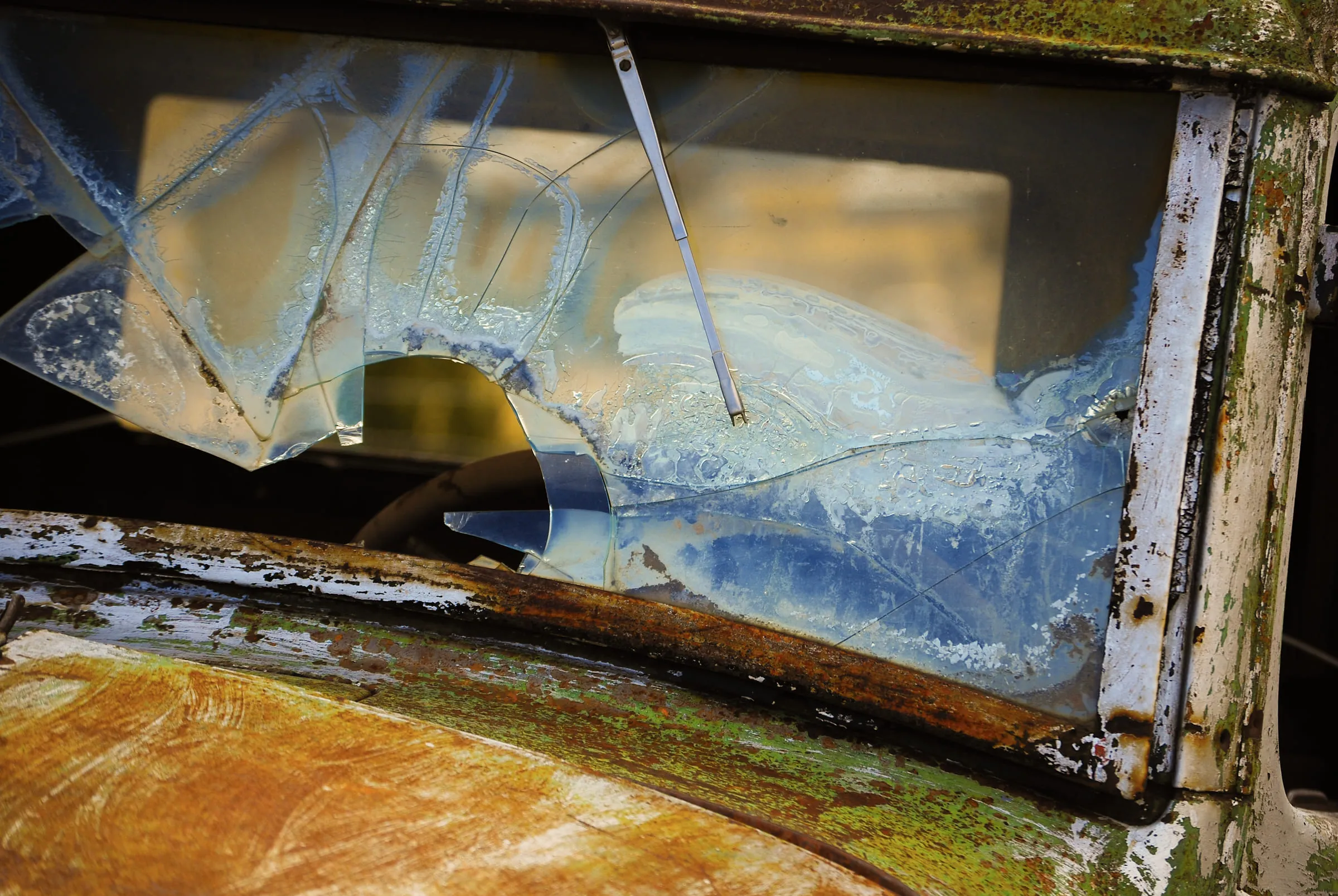 A shattered, opaque windshield in a rusted-out frame, seen from inside a wrecked cab